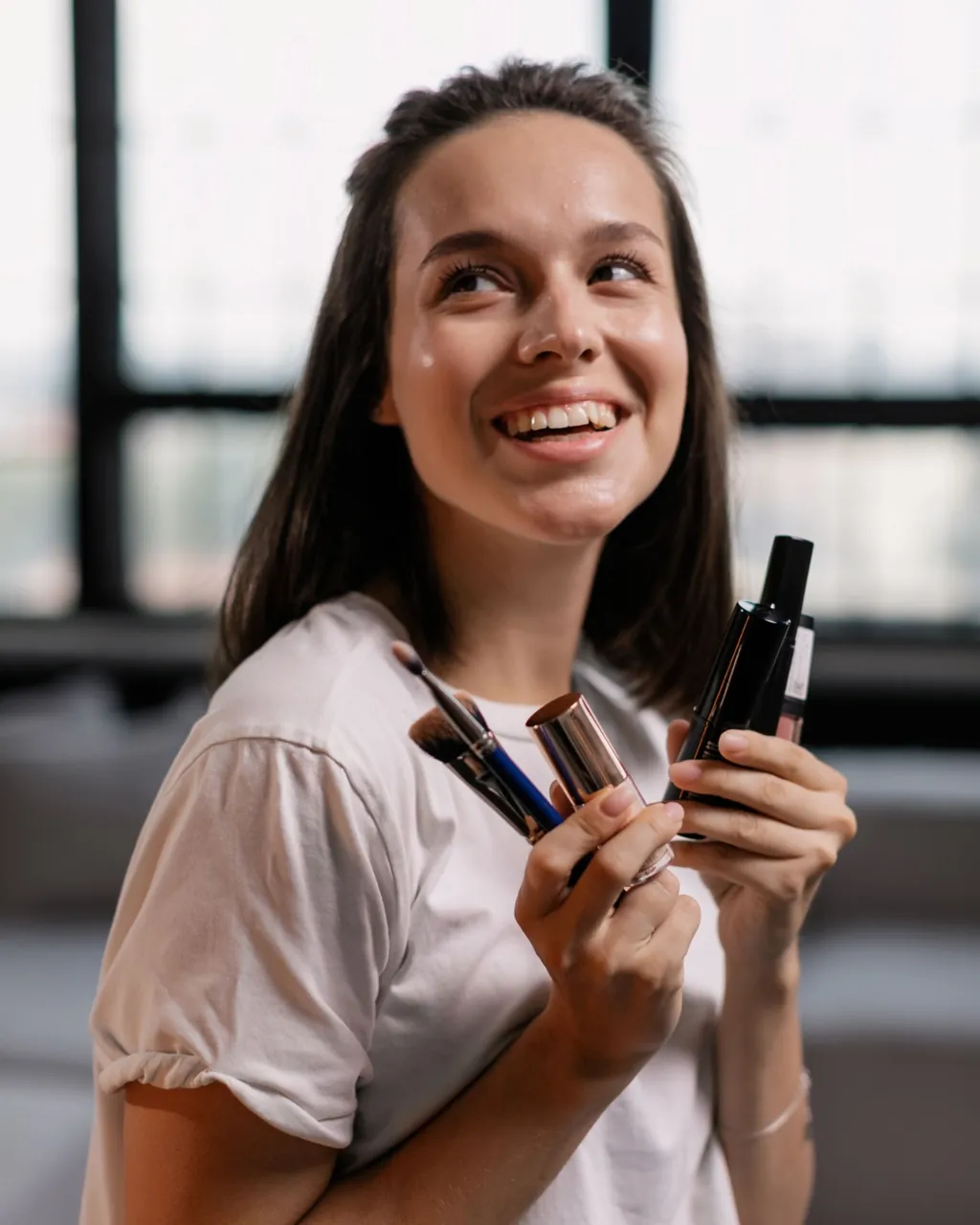 Mulher sorrindo com pincéis, batom e produtos de maquiagem na mão — cosméticos e perfumaria no atacado com a loja B2B VendasxAtacado