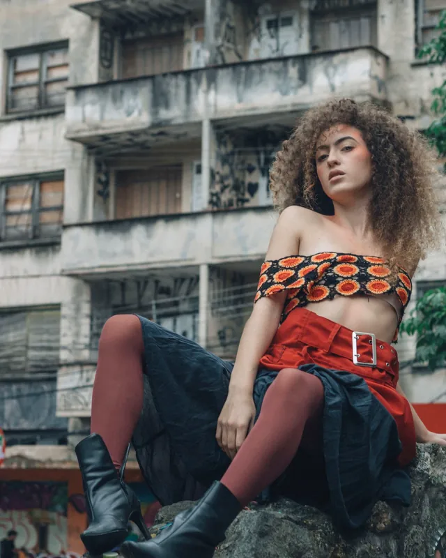 Modelo com top de crochê laranja e preto, saia vermelha com cinto e botas pretas — moda para atacadistas de roupas que vendem no atacado com sua loja B2B VendasxAtacado