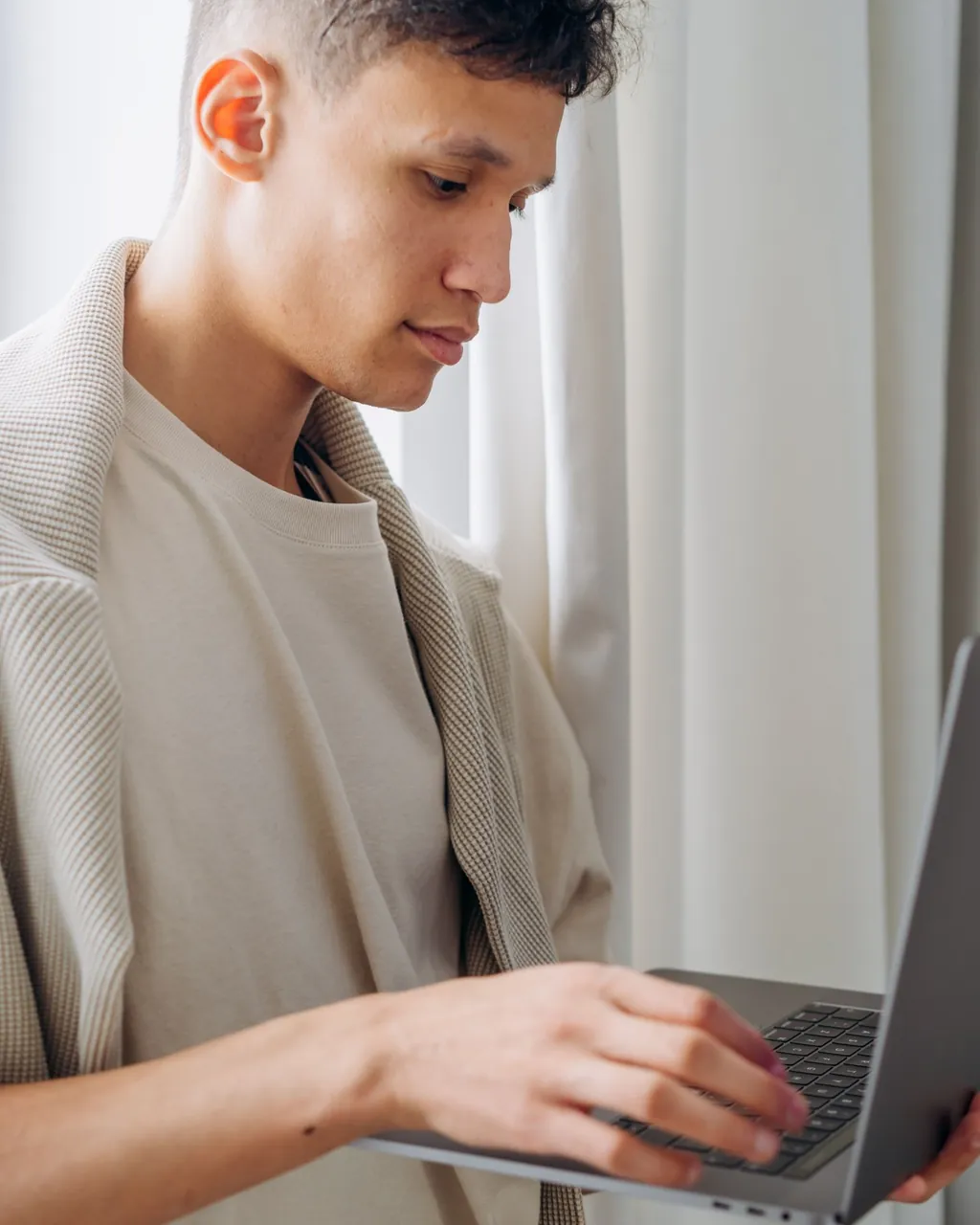 Homem jovem trabalhando em pé com um notebook perto da janela — tecnologia e eletrônicos para distribuidores que vendem no atacado com a loja B2B VendasxAtacado